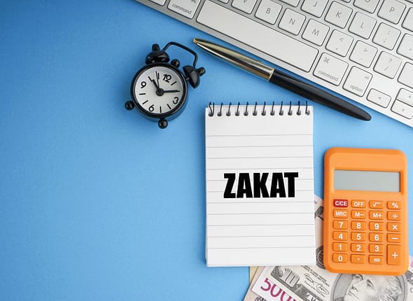 32216008_zakat-or-islamic-tax-on-wealth-text-with-fountain-pen-notepad-banknotes-currency-and-keyboard-on-blue-background (1)